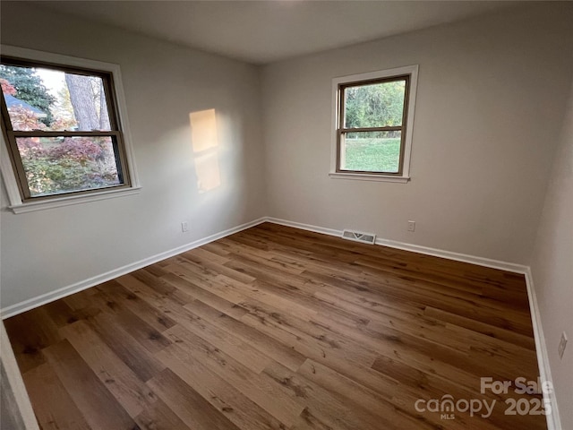 unfurnished room with baseboards, a wealth of natural light, wood finished floors, and visible vents