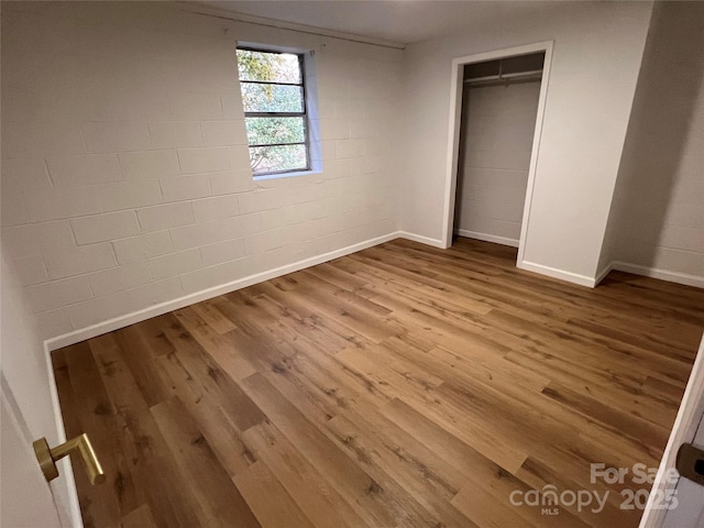 unfurnished bedroom featuring concrete block wall, baseboards, a closet, and wood finished floors