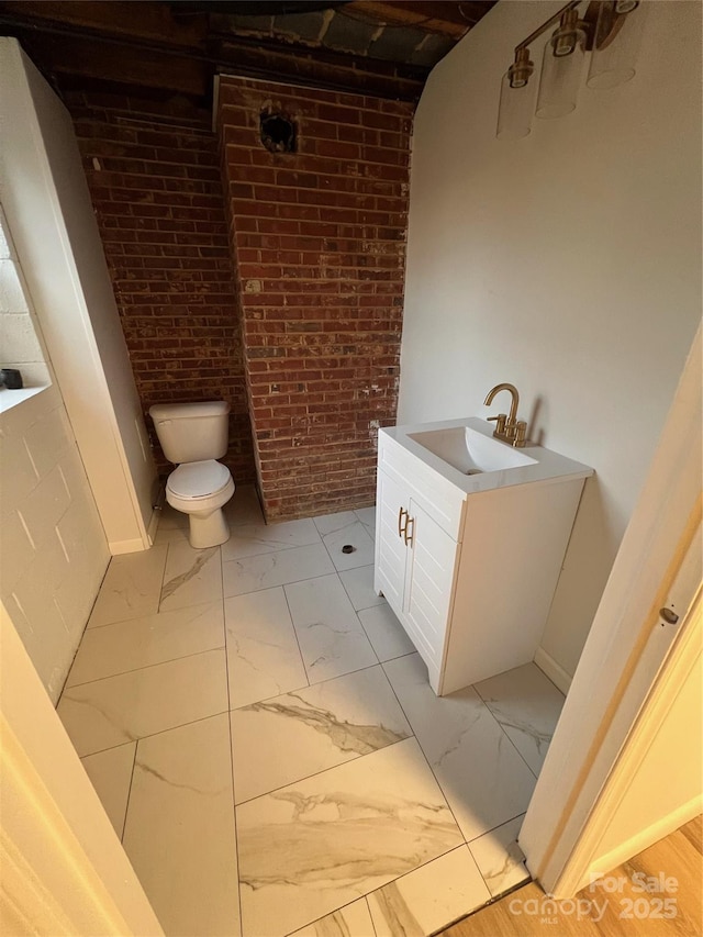 bathroom with vanity, toilet, brick wall, and marble finish floor