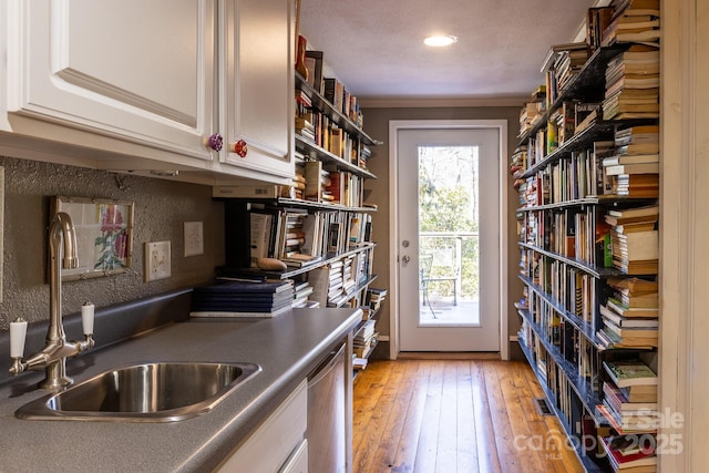 kitchen featuring stainless steel dishwasher, sink, crown molding, light wood-type flooring, and white cabinets