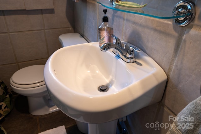 bathroom featuring toilet, tile walls, and sink