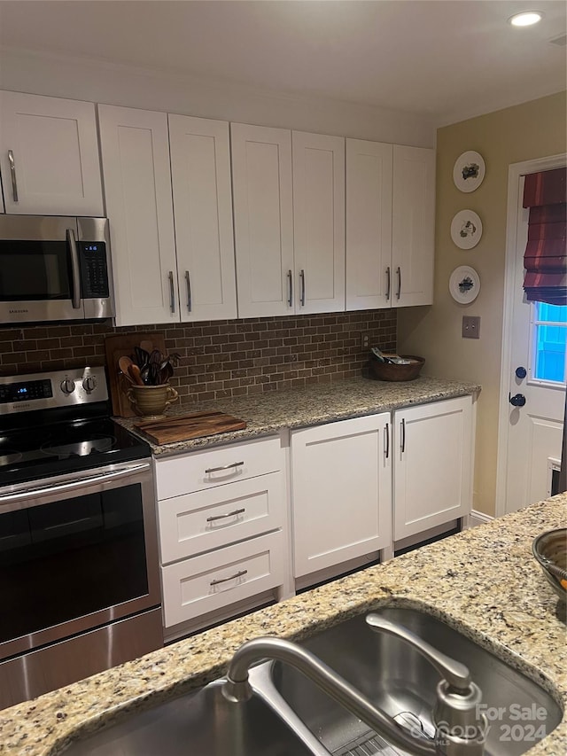 kitchen featuring white cabinets, light stone counters, appliances with stainless steel finishes, and tasteful backsplash