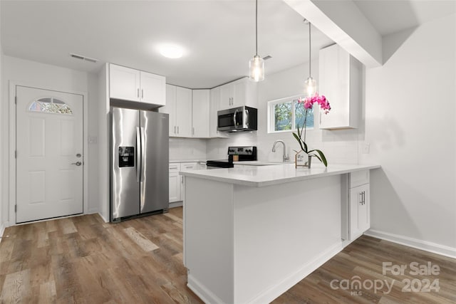 kitchen with hardwood / wood-style floors, kitchen peninsula, tasteful backsplash, white cabinetry, and appliances with stainless steel finishes