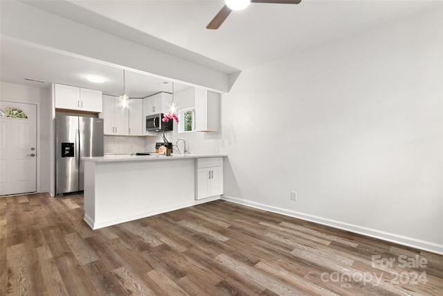 kitchen featuring kitchen peninsula, appliances with stainless steel finishes, decorative light fixtures, white cabinets, and dark hardwood / wood-style flooring