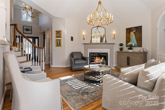 living area featuring stairs, a high end fireplace, an inviting chandelier, and wood finished floors