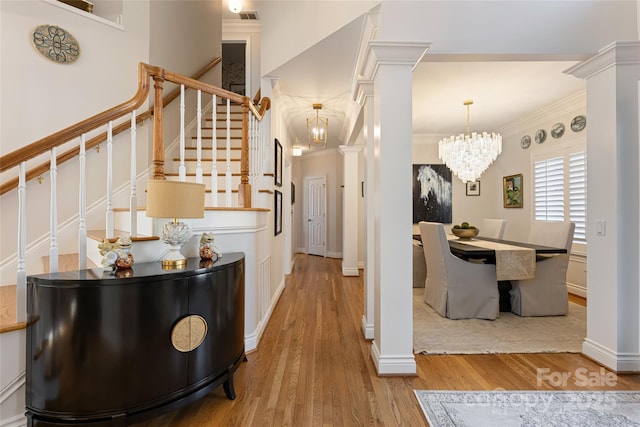 foyer entrance with a notable chandelier, wood finished floors, ornamental molding, stairway, and ornate columns