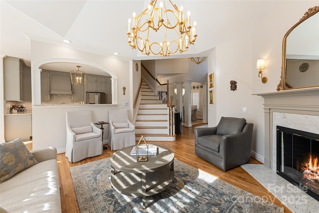 living area featuring a premium fireplace, stairway, wood finished floors, a notable chandelier, and recessed lighting