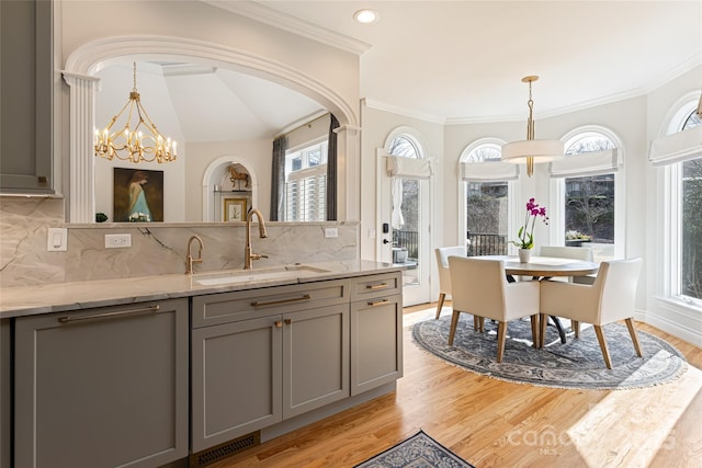 kitchen featuring light wood-style flooring, light stone counters, a sink, gray cabinets, and a notable chandelier