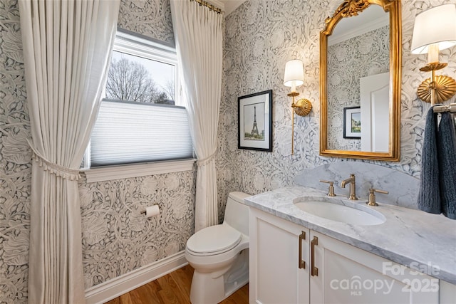 bathroom with vanity, wood finished floors, toilet, and wallpapered walls