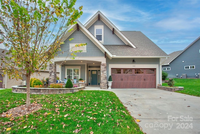 craftsman house with central AC unit, a front yard, covered porch, and a garage