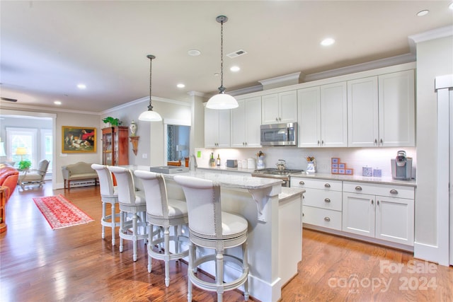 kitchen with white cabinets, stainless steel appliances, a center island with sink, and decorative light fixtures