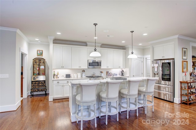 kitchen featuring stainless steel appliances, hanging light fixtures, white cabinets, dark wood-type flooring, and a kitchen island with sink