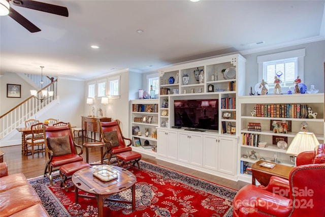 living room featuring hardwood / wood-style floors, ceiling fan with notable chandelier, and crown molding