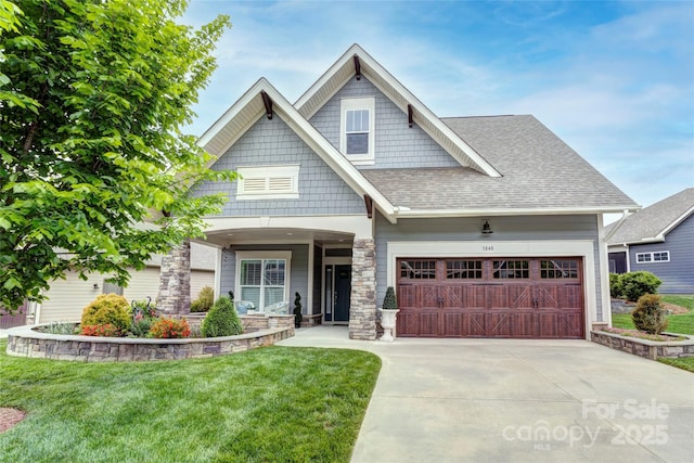 craftsman-style house with roof with shingles, a front lawn, driveway, and stone siding