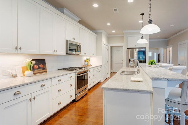 kitchen featuring stainless steel appliances, a sink, visible vents, a kitchen breakfast bar, and crown molding