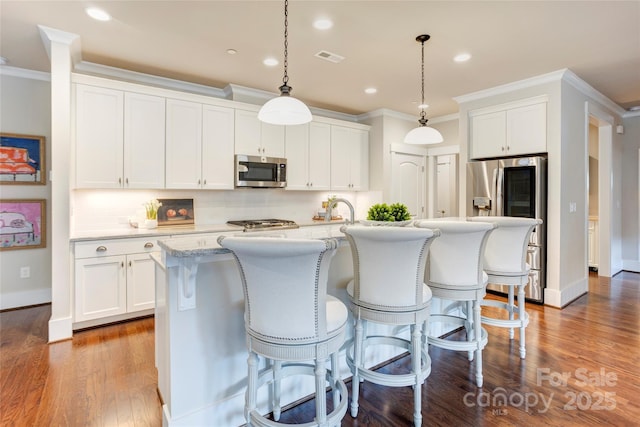 kitchen with tasteful backsplash, an island with sink, appliances with stainless steel finishes, white cabinets, and ornamental molding
