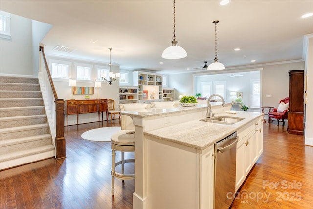 kitchen featuring white cabinets, a sink, dishwasher, wood finished floors, and a center island with sink