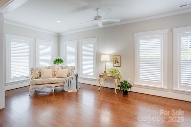 living area featuring crown molding, visible vents, ceiling fan, baseboards, and wood finished floors