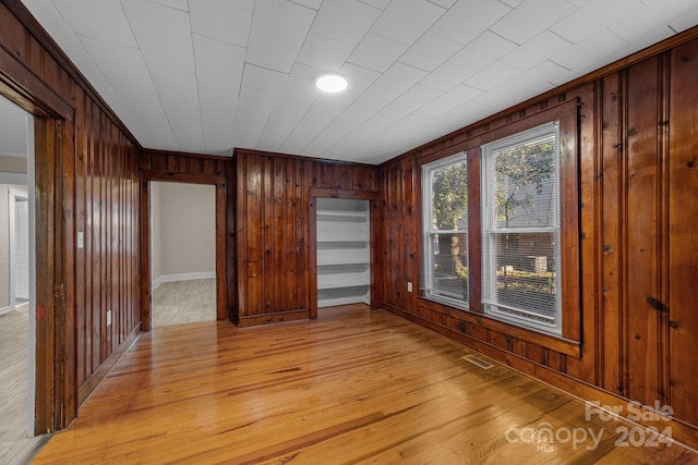 unfurnished room featuring ornamental molding, light wood-type flooring, and wooden walls