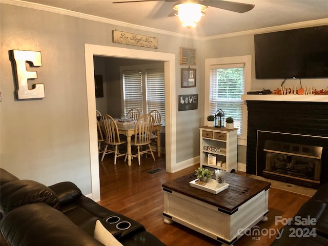 living room featuring dark wood-type flooring, a brick fireplace, ceiling fan, and crown molding