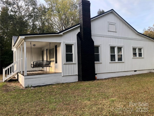view of side of home with a lawn, a chimney, crawl space, and a porch