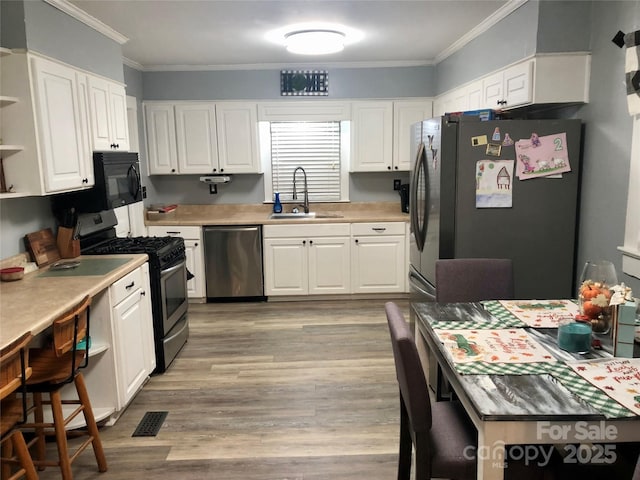 kitchen featuring white cabinets, ornamental molding, appliances with stainless steel finishes, a sink, and open shelves