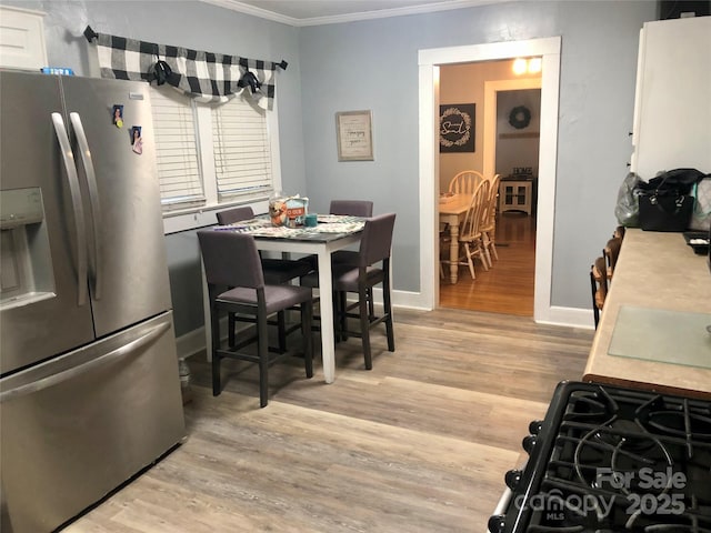 kitchen with baseboards, crown molding, light wood-style floors, and stainless steel refrigerator with ice dispenser