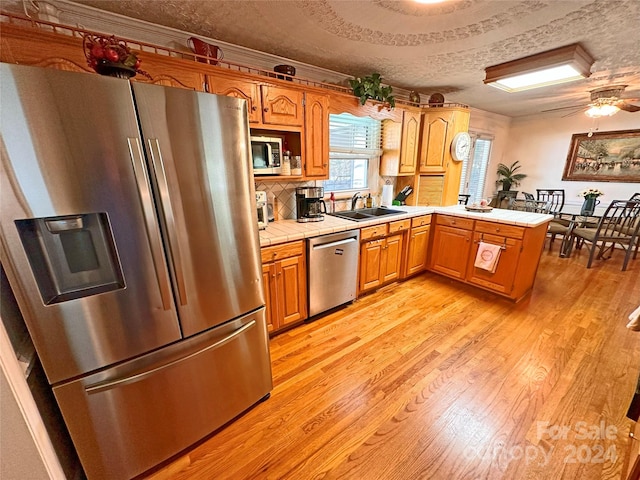 kitchen featuring tile counters, kitchen peninsula, a textured ceiling, appliances with stainless steel finishes, and light wood-type flooring