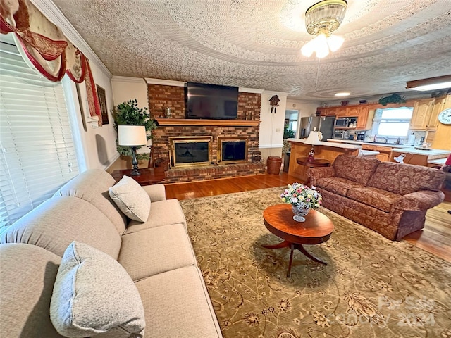 living room featuring a fireplace, ceiling fan, a textured ceiling, and light hardwood / wood-style flooring