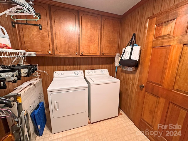 clothes washing area with washing machine and dryer, wood walls, and cabinets