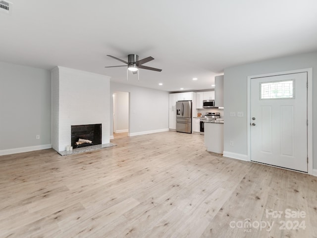 unfurnished living room featuring a brick fireplace, light wood-type flooring, and ceiling fan