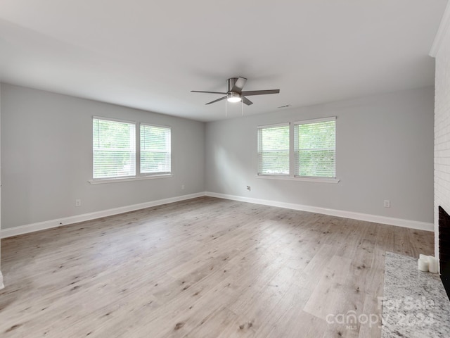 spare room featuring ceiling fan, light hardwood / wood-style floors, and a brick fireplace