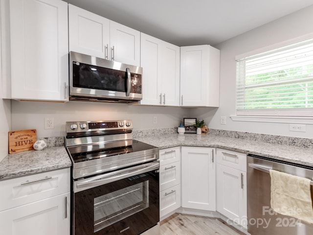 kitchen featuring stainless steel appliances, white cabinets, light wood-type flooring, and light stone counters