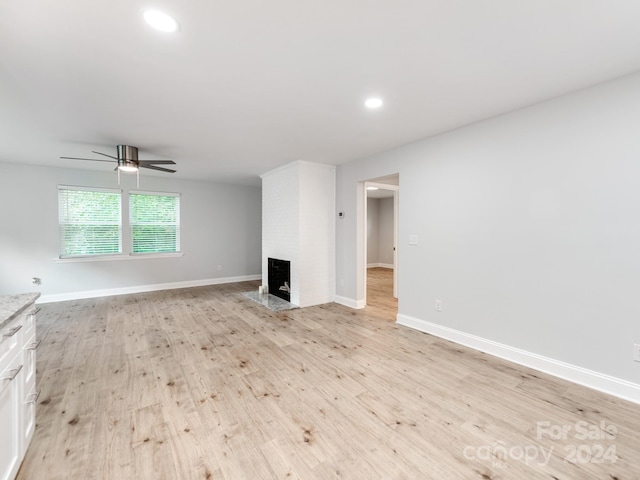 unfurnished living room featuring a brick fireplace, ceiling fan, and light wood-type flooring