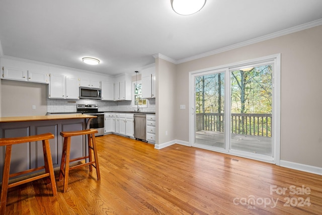 kitchen with crown molding, white cabinetry, appliances with stainless steel finishes, light wood-type flooring, and decorative backsplash