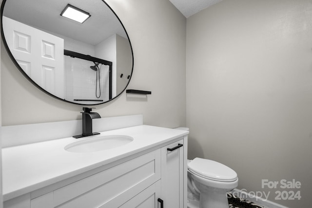 bathroom with toilet, vanity, a textured ceiling, and a shower with door