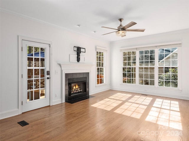 unfurnished living room with ornamental molding, a tiled fireplace, hardwood / wood-style flooring, and ceiling fan