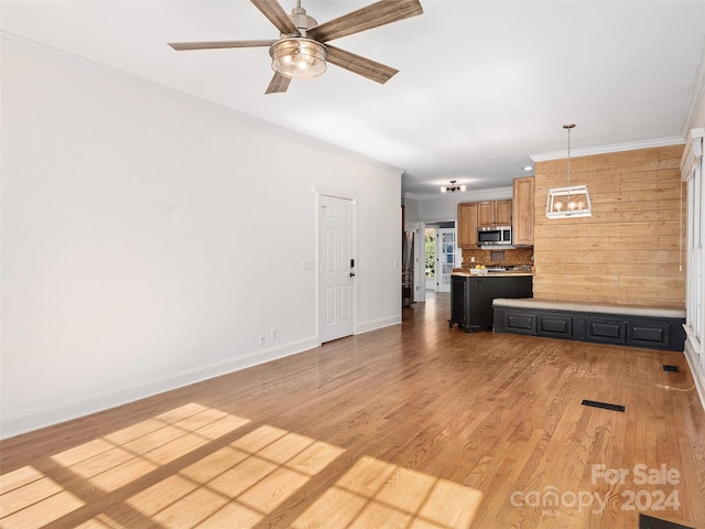 unfurnished living room featuring ornamental molding, ceiling fan with notable chandelier, light hardwood / wood-style flooring, and wood walls