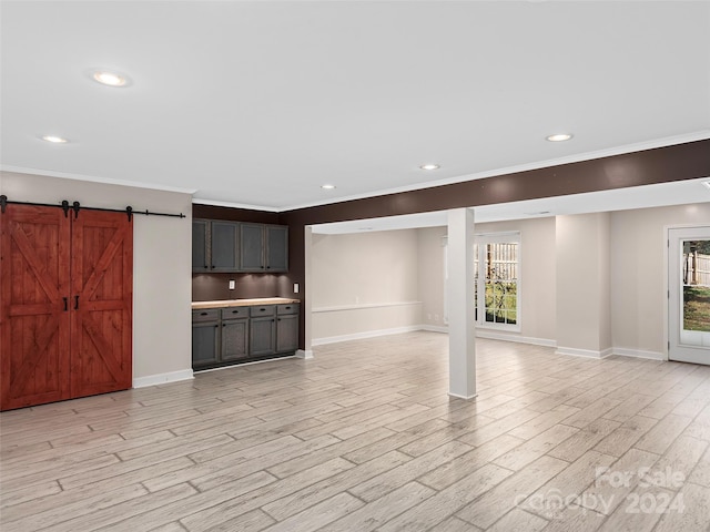 unfurnished living room with a barn door, ornamental molding, and light hardwood / wood-style flooring