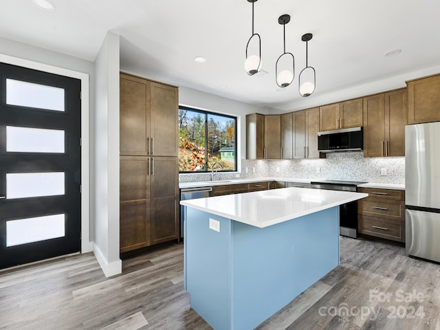 kitchen featuring stainless steel appliances, a center island, decorative backsplash, hanging light fixtures, and light wood-type flooring