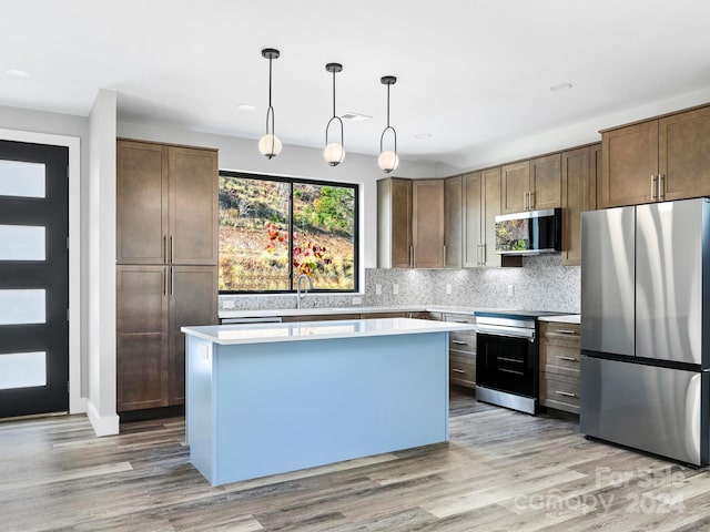 kitchen featuring tasteful backsplash, stainless steel appliances, a kitchen island, decorative light fixtures, and light hardwood / wood-style floors