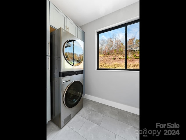 laundry room with cabinets, stacked washing maching and dryer, and light tile patterned floors