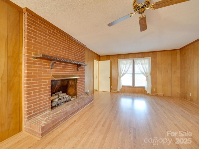 unfurnished living room with a textured ceiling, light hardwood / wood-style flooring, a brick fireplace, and wood walls