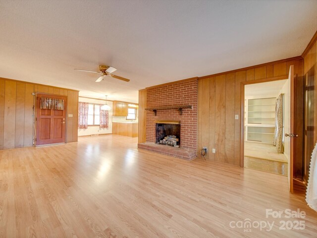 unfurnished living room featuring a fireplace, light hardwood / wood-style floors, ceiling fan, and wood walls