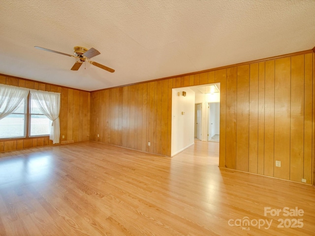 spare room featuring wood walls, ceiling fan, light hardwood / wood-style floors, and a textured ceiling