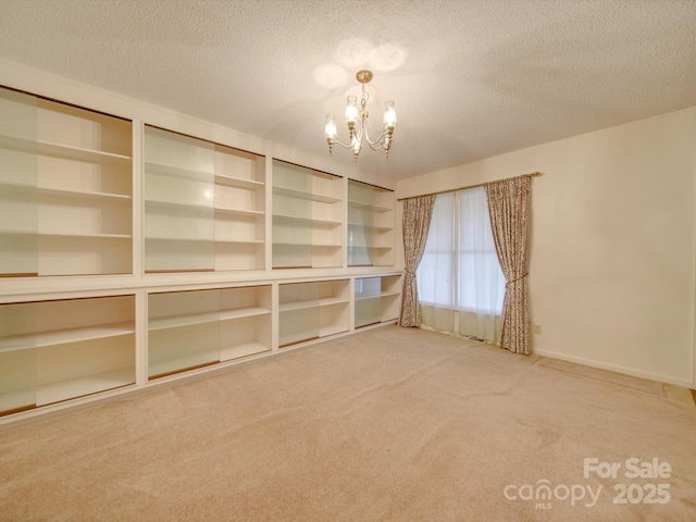 spare room featuring carpet flooring, a chandelier, and a textured ceiling