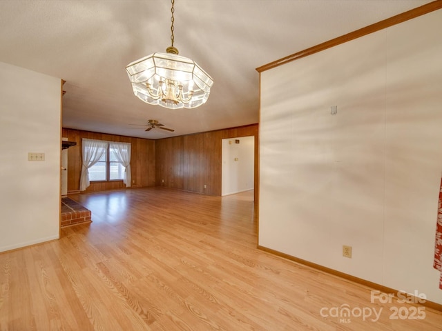 unfurnished room featuring wooden walls, ceiling fan with notable chandelier, and light wood-type flooring