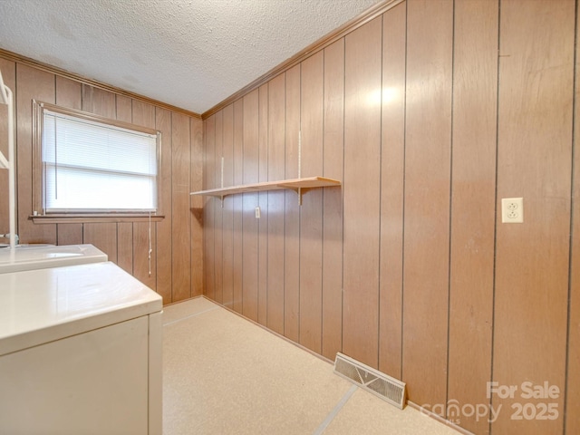 laundry area with a textured ceiling, wooden walls, and washing machine and clothes dryer