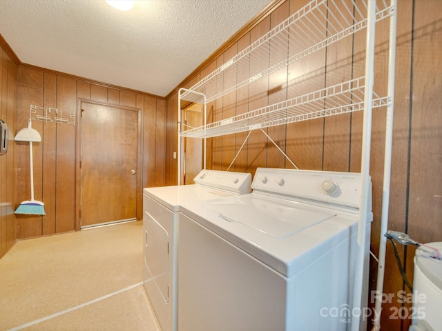 clothes washing area featuring a textured ceiling, washer and clothes dryer, and wooden walls