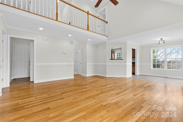 unfurnished living room with ceiling fan, light wood-type flooring, high vaulted ceiling, and ornamental molding